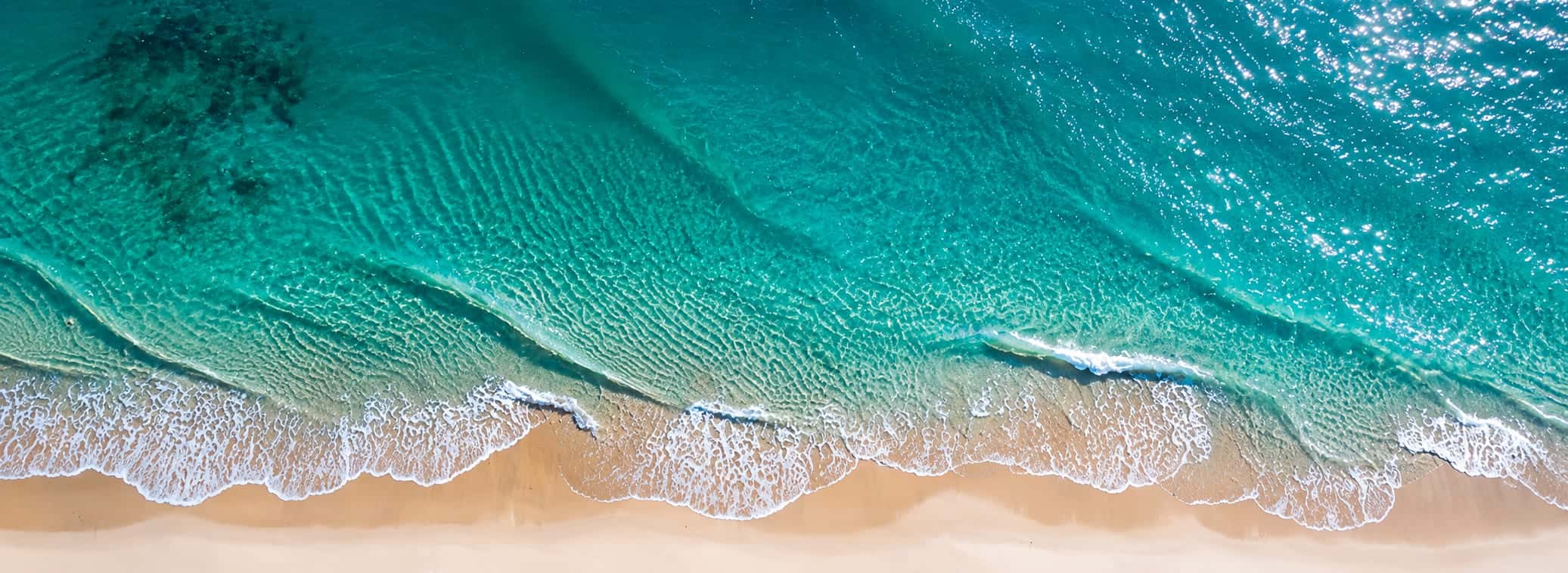 Aerial view of a Cairns beach, with turquoise water meeting a sandy shoreline